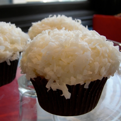 A photo coconut cake, cream cheese frosting topped with coconut cupcakes.